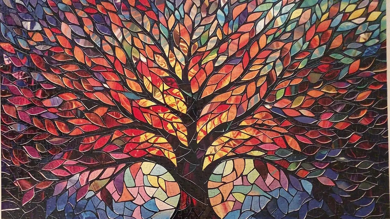 The finished Pickforu Mosaic Tree of Life puzzle, a stained glass tree in dark leading, its canopy running from reds and golds at the center out to blues, teals and purples at the edges, with two pale circular forms low against a near black ground.